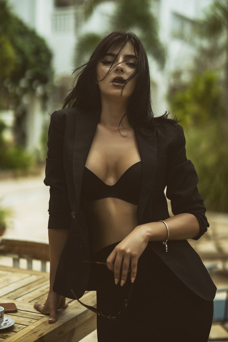 Fashionable woman in black suit and bra posing in a tropical setting, exuding confidence.